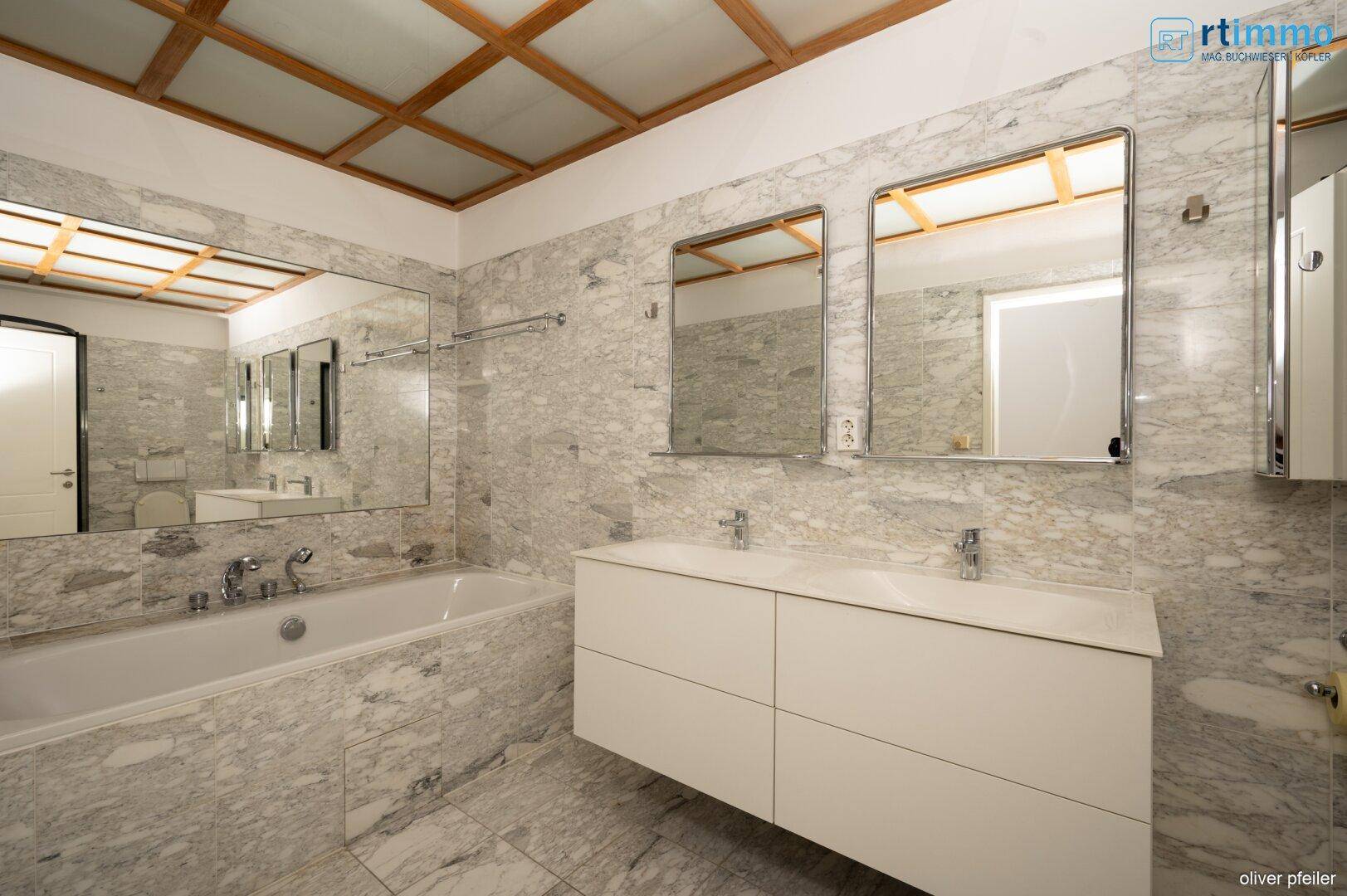 Elegantes Badezimmer mit Marmorfliesen, Doppelwaschbecken und integrierter Badewanne.