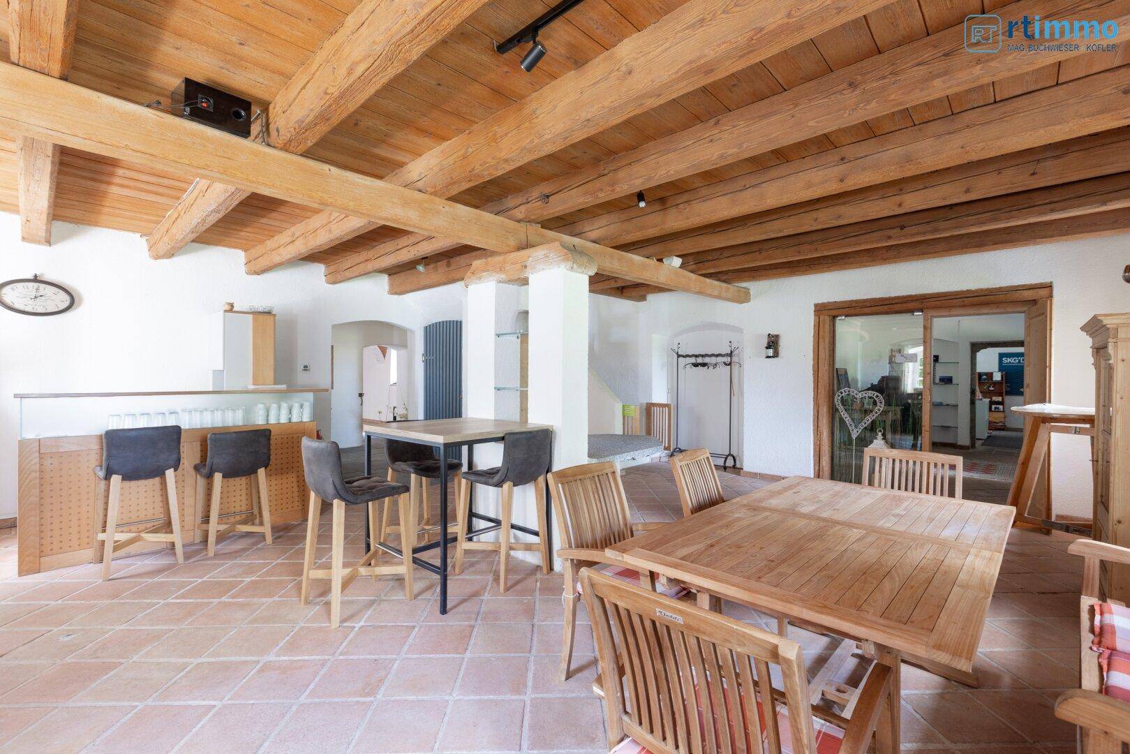 Rustikaler Essbereich mit Holztischen, Barhockern und sichtbaren Holzbalken an der Decke.