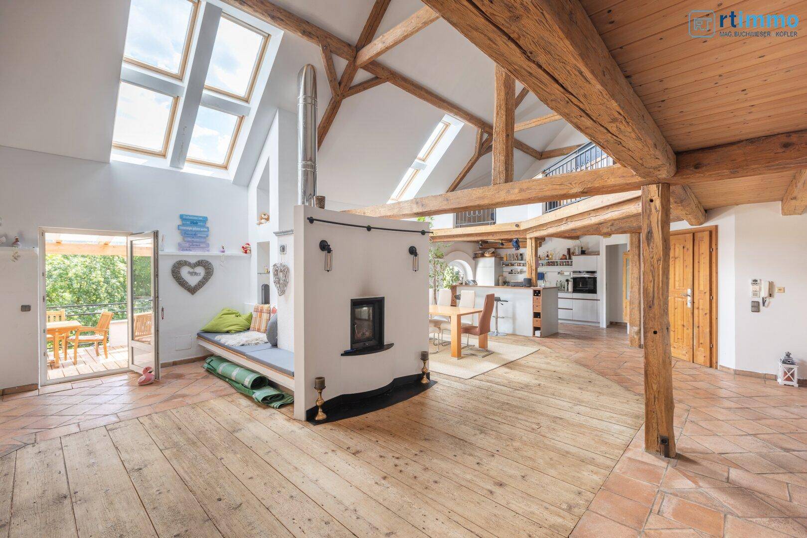 Heller, offener Wohnbereich mit Kachelofen, Holzboden, Dachfenstern und Zugang zur Terrasse.