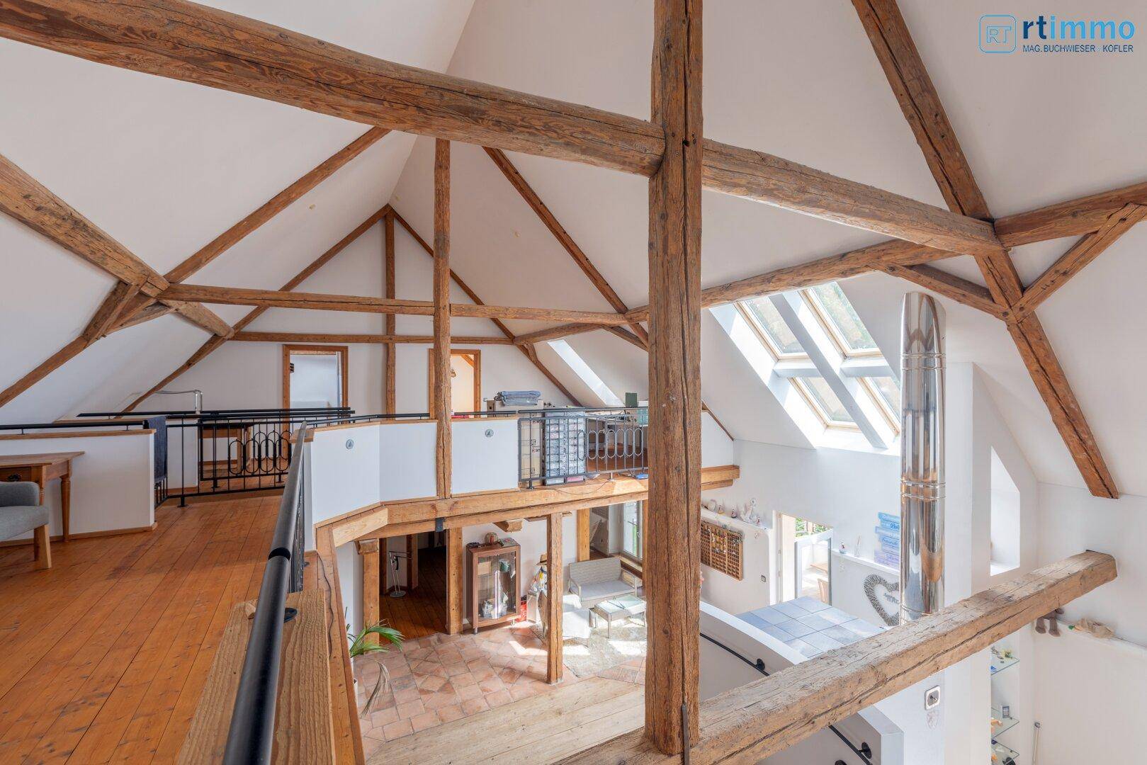 Offener Loftbereich mit hohen Decken, sichtbaren Holzbalken und Dachfenstern für viel Licht.