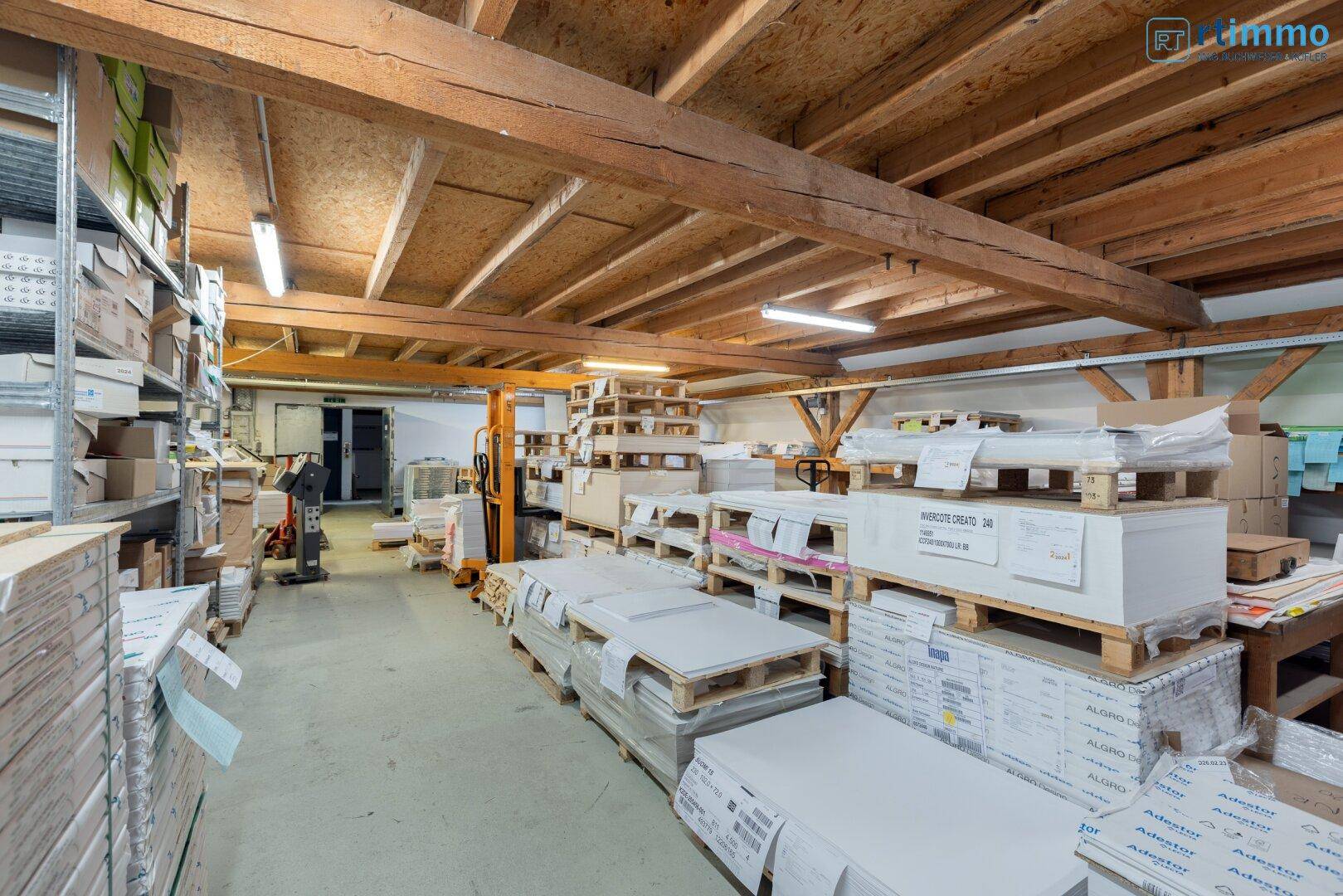 Lagerraum mit Holzbalkendecke, Paletten voller Material und Regalsystemen.