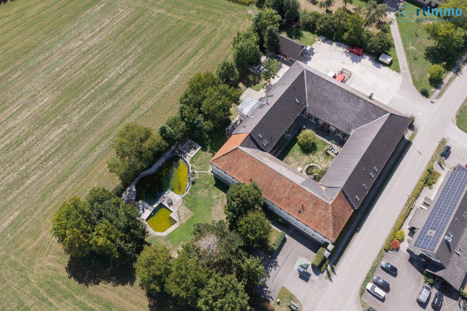 Vogelperspektive des U-förmigen Gebäudekomplexes mit Innenhof und angrenzendem Teichbereich.