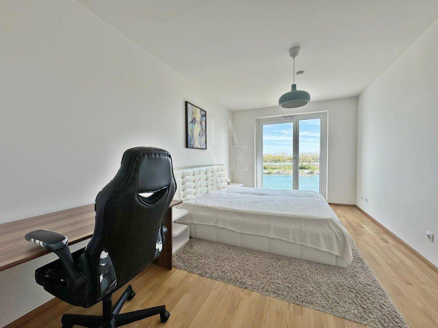 Schlafzimmer mit Seeblick, Holzboden und direktem Zugang zum Balkon.