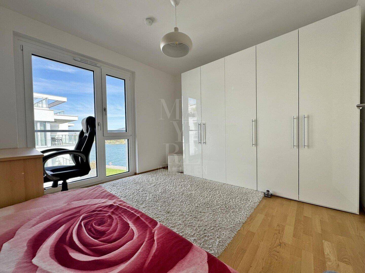 Schlafzimmer mit weißem Kleiderschrank, Holzboden und Fenster mit Seeblick.