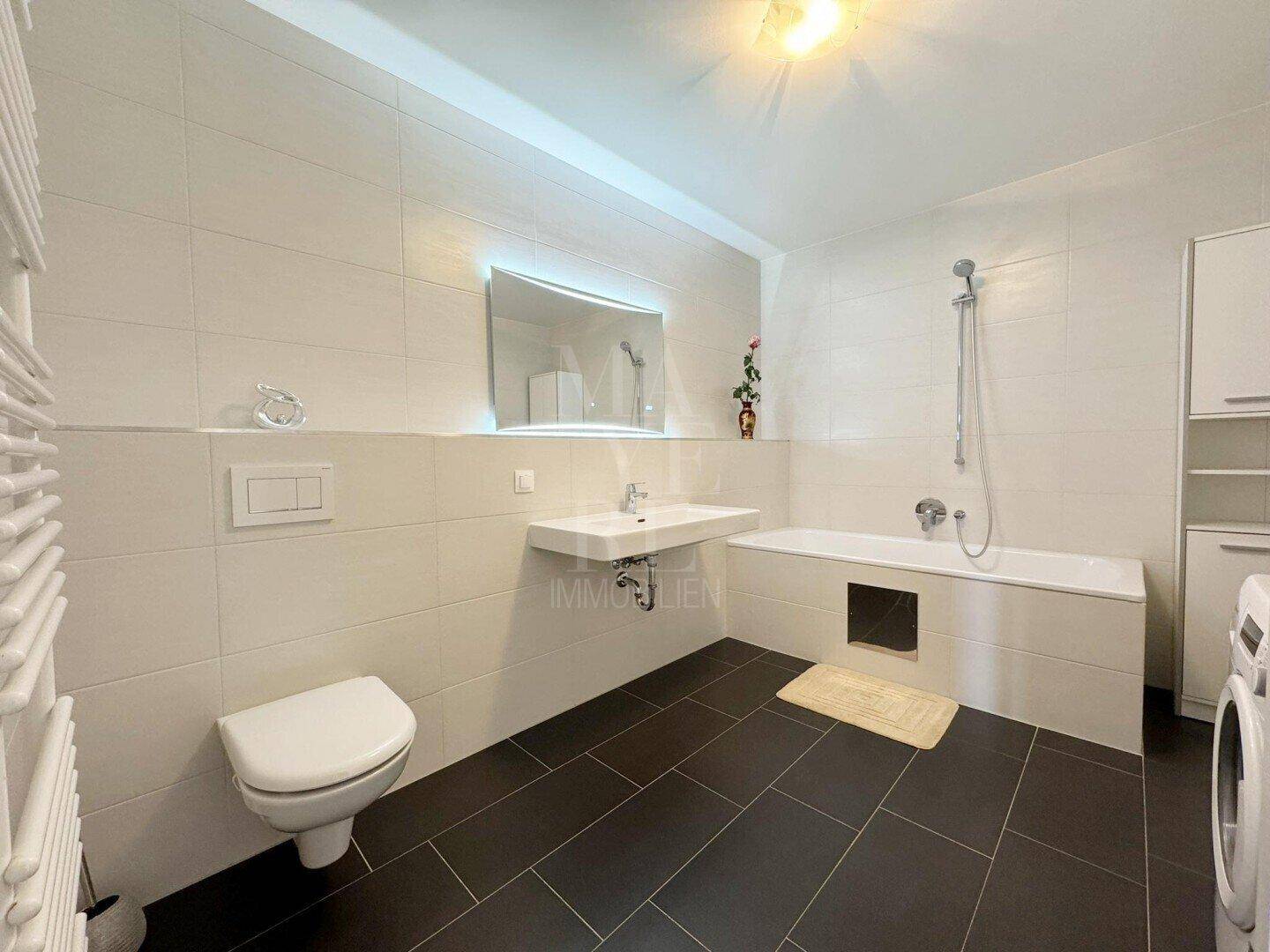 Modernes Badezimmer mit Badewanne, WC, Einzelwaschbecken und Fliesenboden.