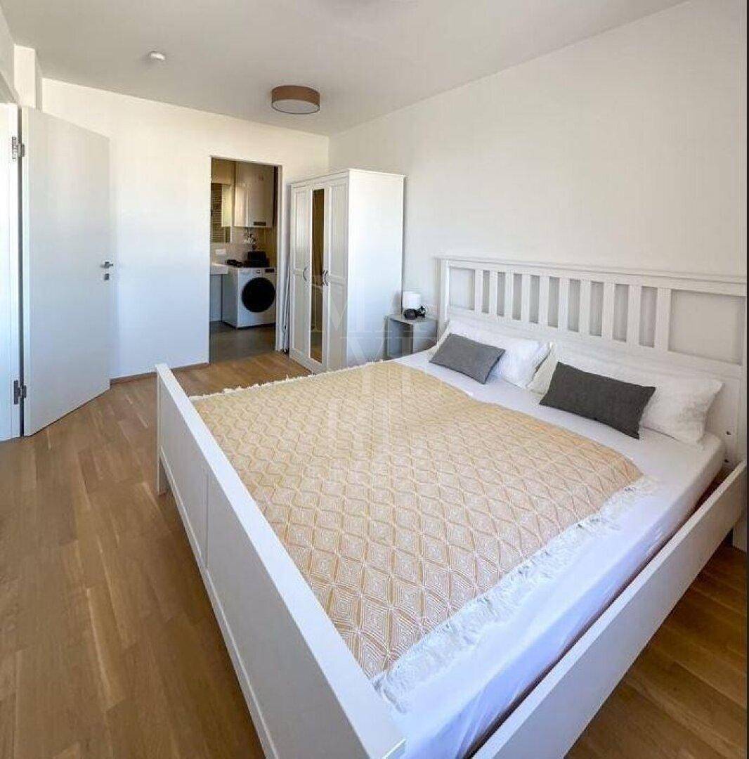 Helles Schlafzimmer mit weißem Bett, Holzboden und Zugang zu einem praktischen Nebenraum.