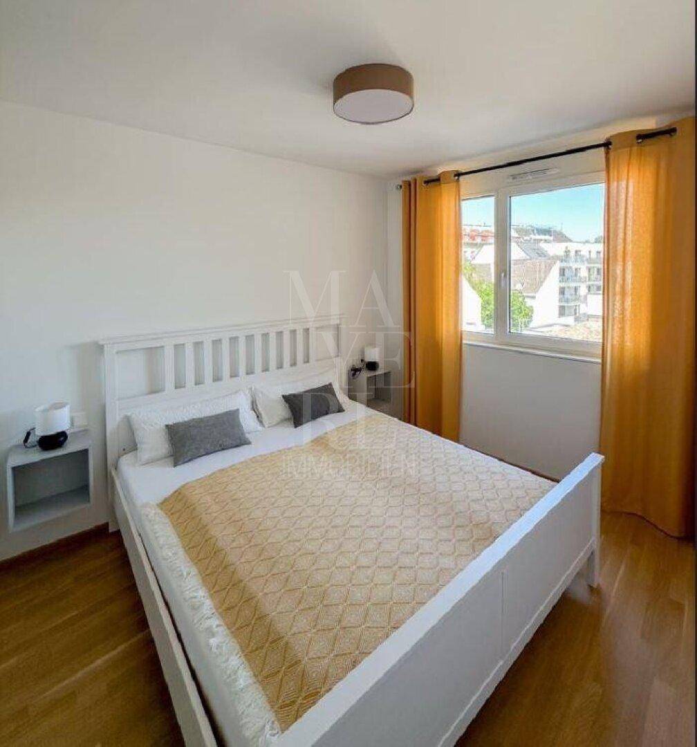 Schlafzimmer mit weißem Bett, Holzboden und Fenster mit Blick ins Grüne und auf die Umgebung.
