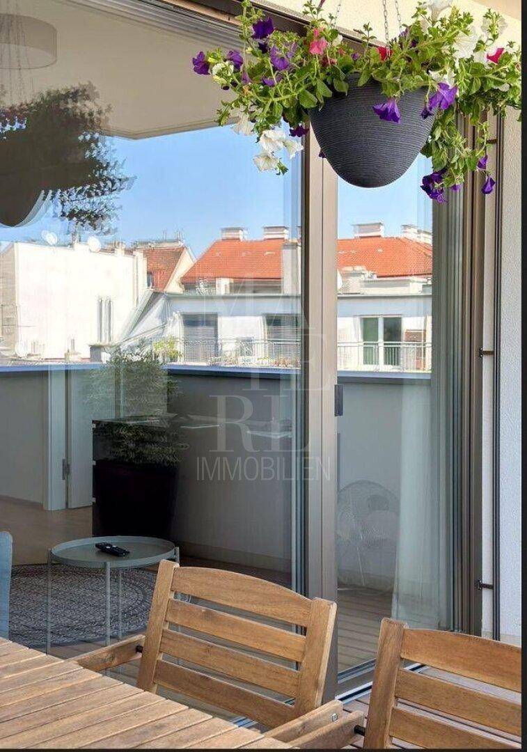 Blick vom Wohnbereich auf den Balkon mit Stadtansicht, Blumen und viel Tageslicht.