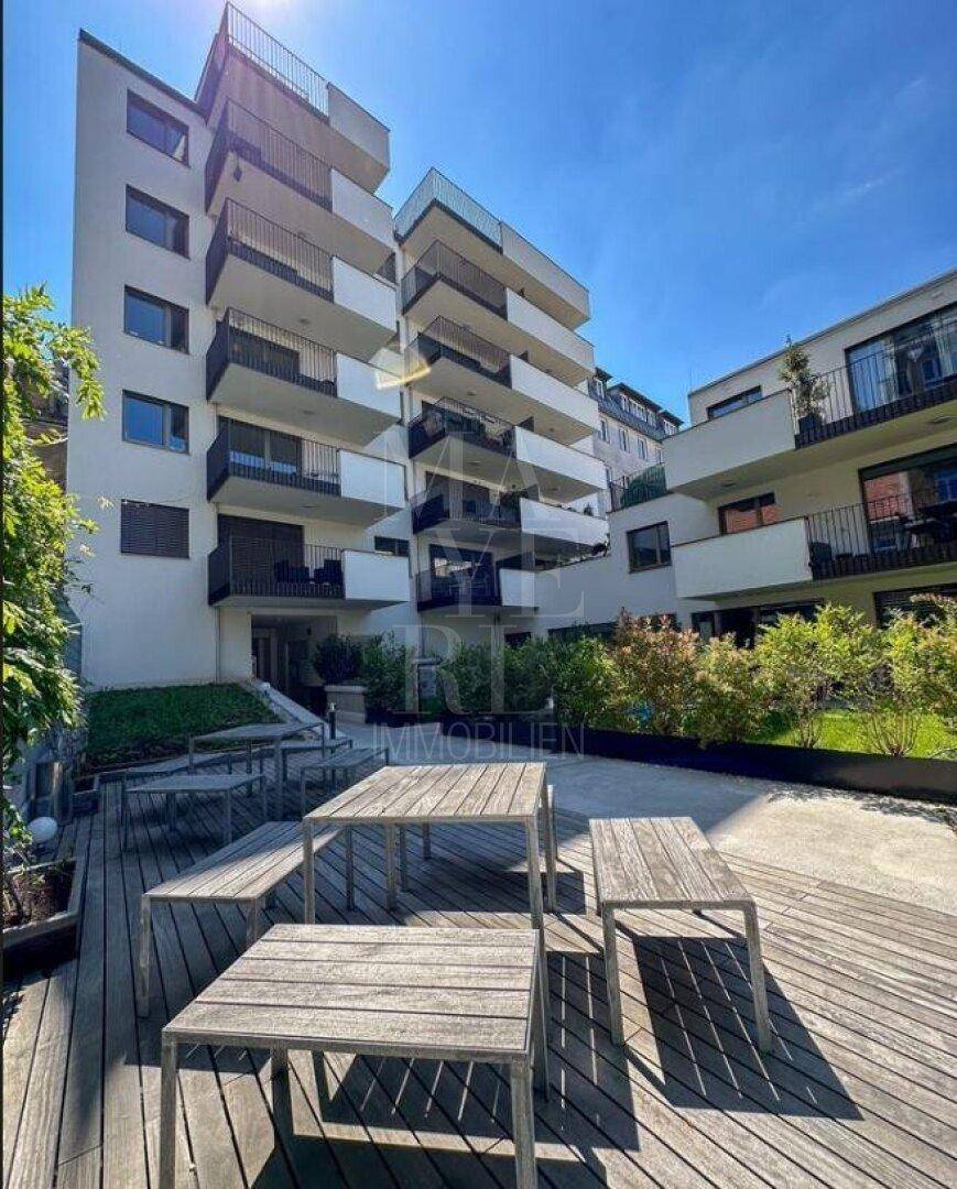 Moderne Wohnanlage mit mehreren Balkonen und einem gemeinschaftlichen Außenbereich mit Sitzgelegenheiten.