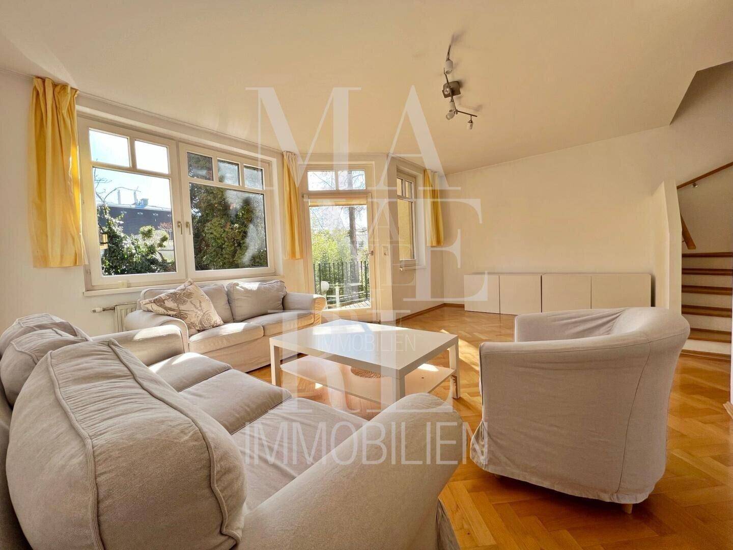 Helles Wohnzimmer mit Parkettboden, bequemen Sofas und Zugang zu einem kleinen Balkon.