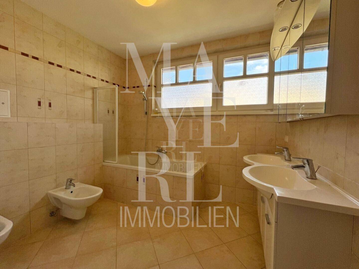 Badezimmer mit beigefarbenen Fliesen, Doppelwaschbecken, Badewanne und Bidet.