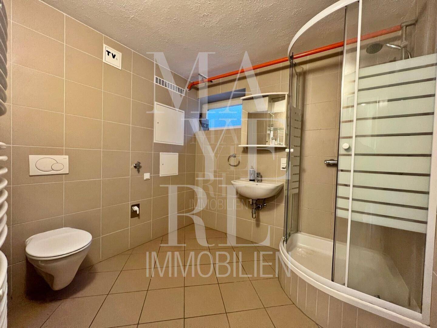 Modernes Badezimmer mit beigefarbenen Fliesen, Duschkabine und wandhängendem WC.