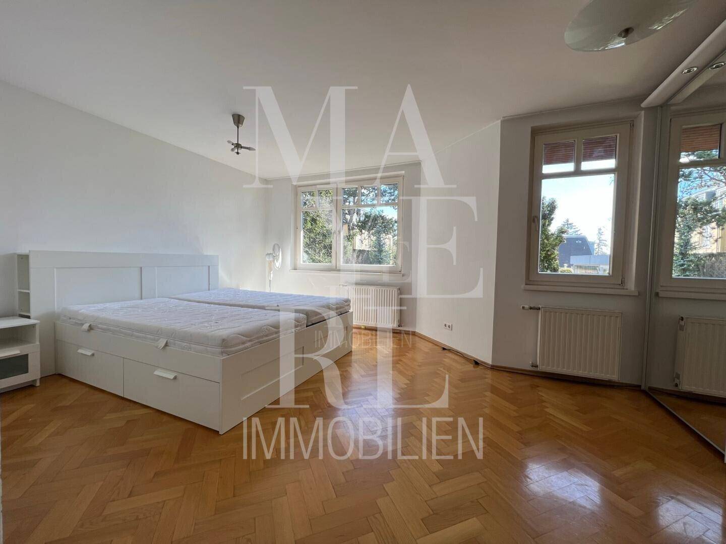 Geräumiges Schlafzimmer mit Parkettboden, Doppelbett und Spiegelschrank, gut beleuchtet durch große Fenster.