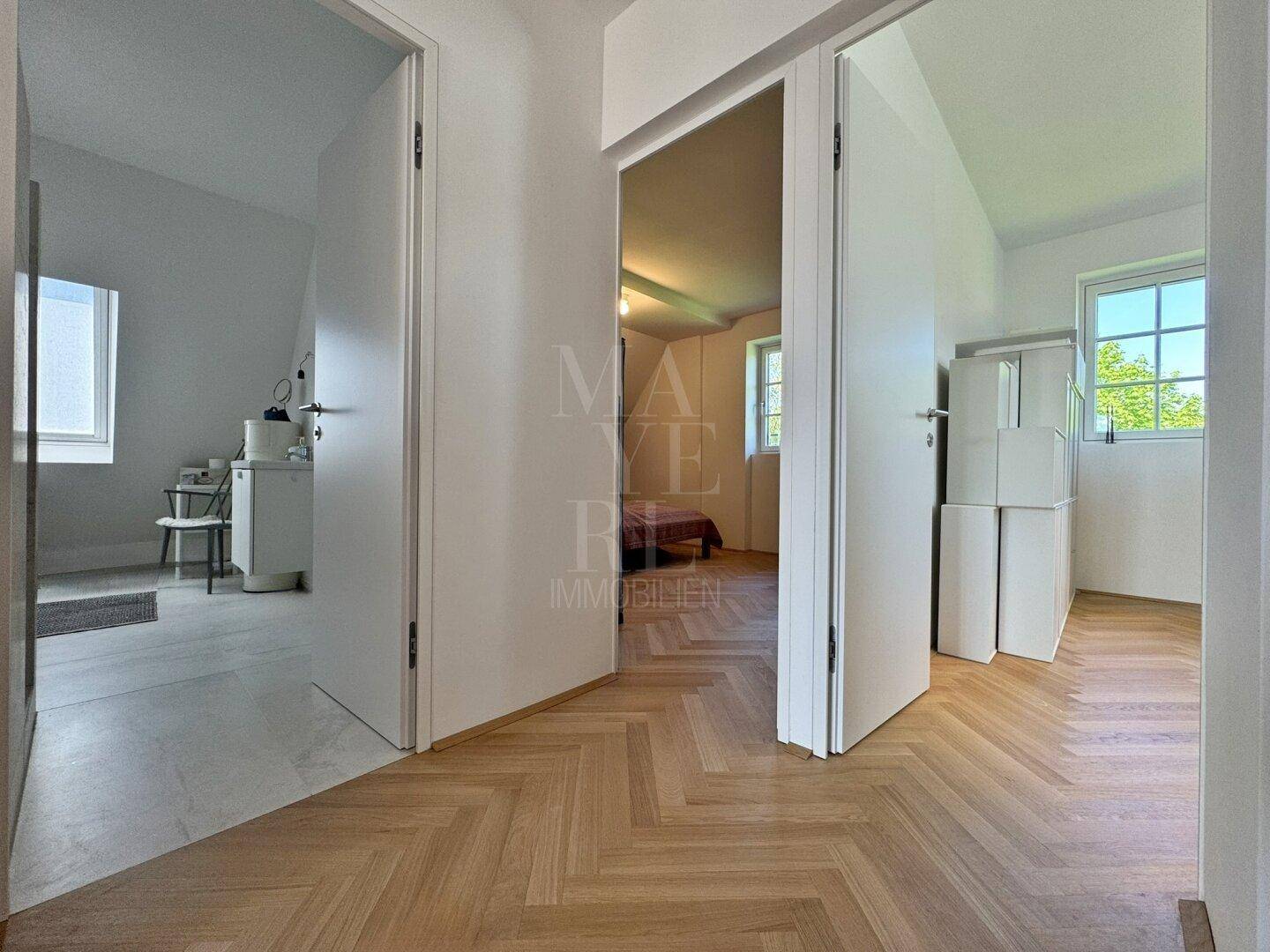 Heller Flur mit elegantem Fischgrätparkett und offenen Durchgängen zu weiteren Räumen.
