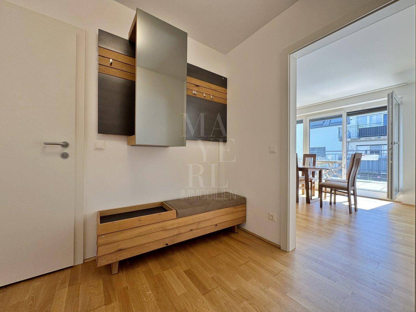 Heller Flur mit Garderobe und Blick in den Essbereich mit Zugang zu einem Balkon.