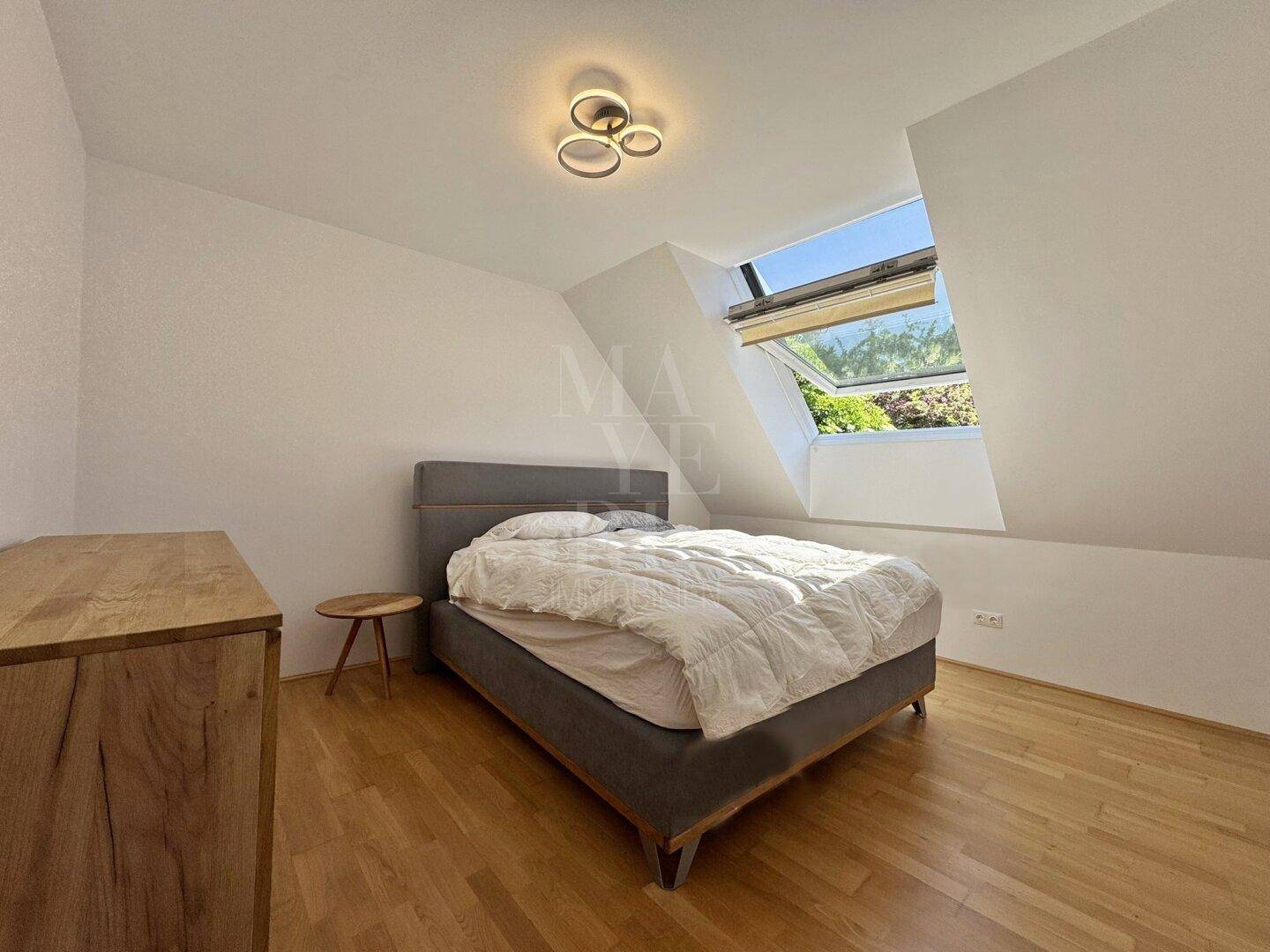 Helles Schlafzimmer mit Holzboden, modernem Bett und großem Dachfenster für viel Tageslicht.
