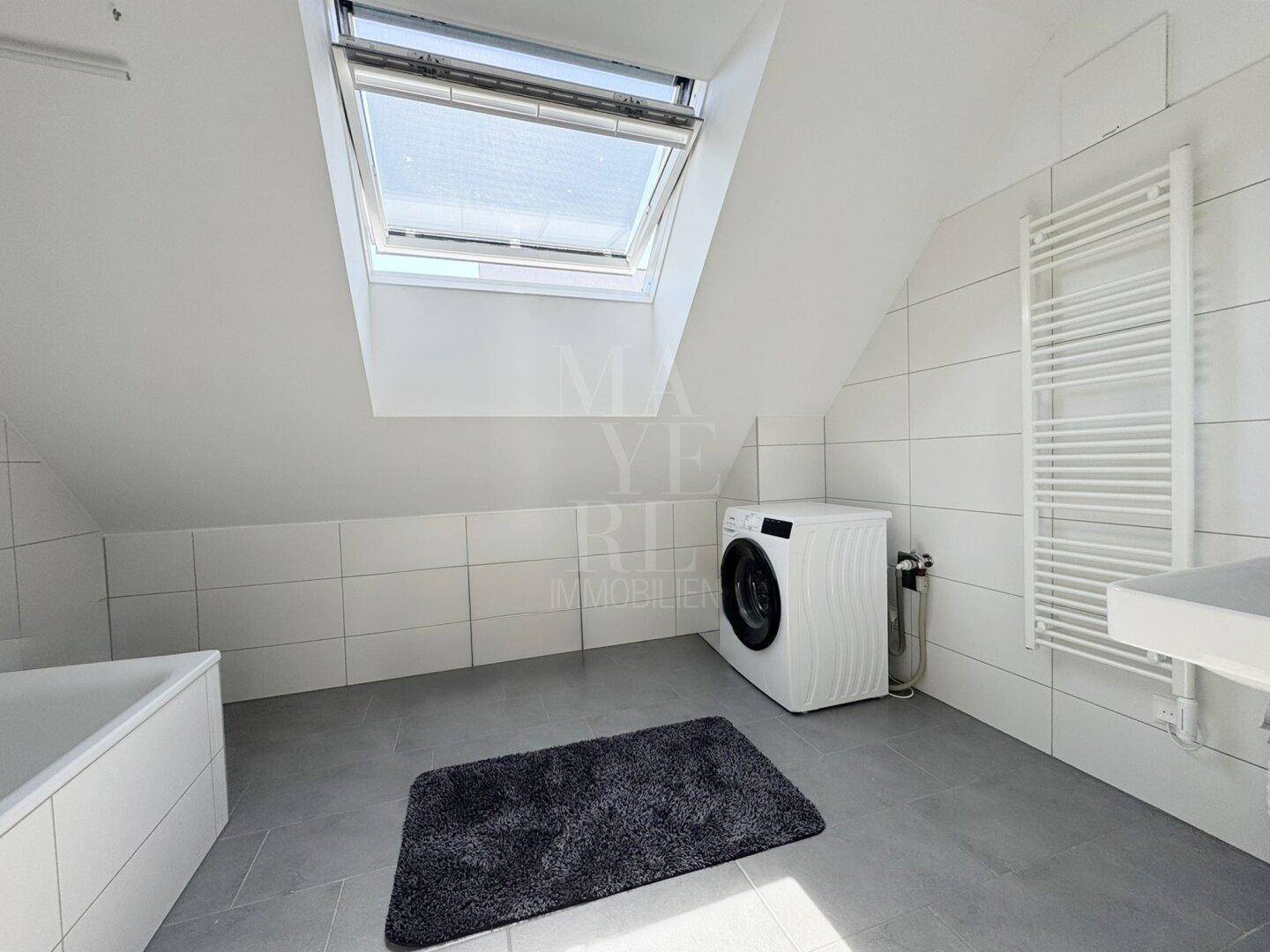 Modernes Badezimmer mit Badewanne, Waschmaschine, Handtuchheizkörper und großem Dachfenster.