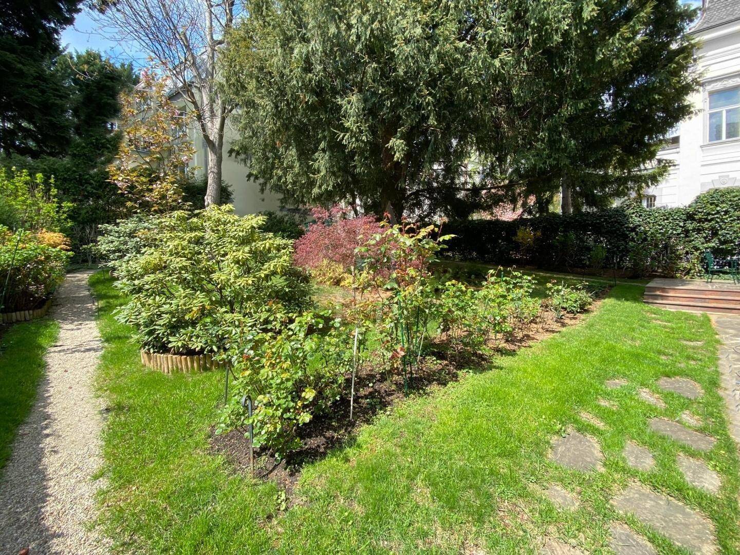 Gepflegter Gartenbereich mit Rasenflächen, verschiedenen Pflanzen und einem Kiesweg.