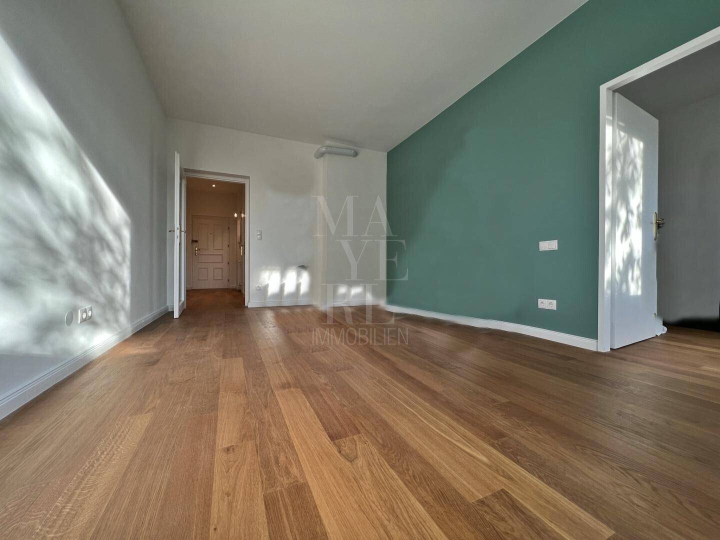 Helles Zimmer mit Holzboden und einer Akzentwand in Grün, bereit zur individuellen Gestaltung.
