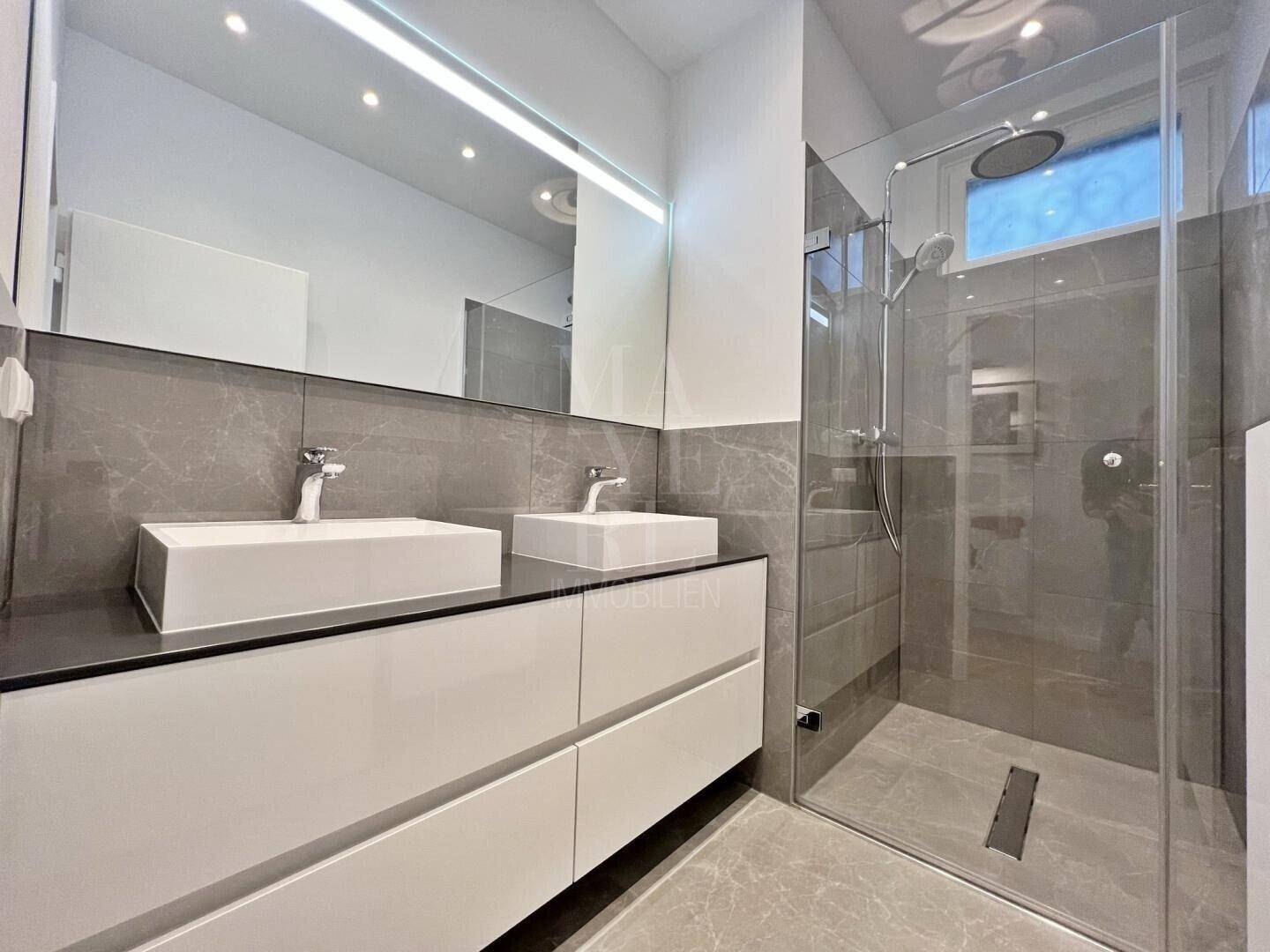 Modernes Badezimmer mit Doppelwaschbecken, großer begehbarer Dusche und grauen Fliesen.