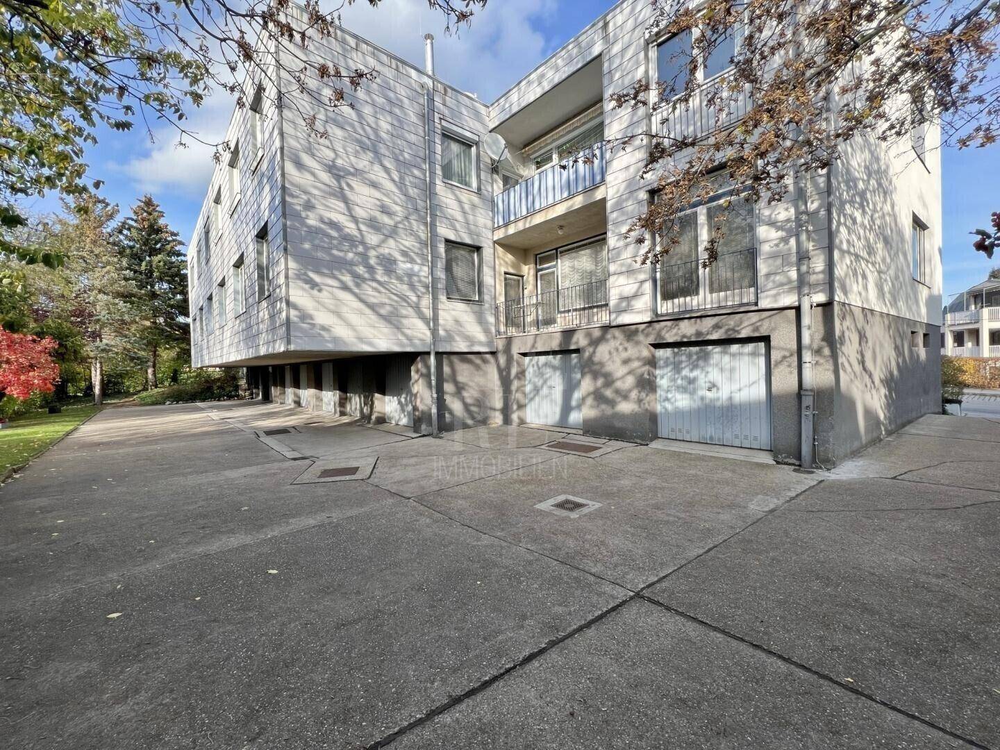 Mehrfamilienhaus mit Garagenzugang und gepflegter Außenanlage an einem sonnigen Tag.