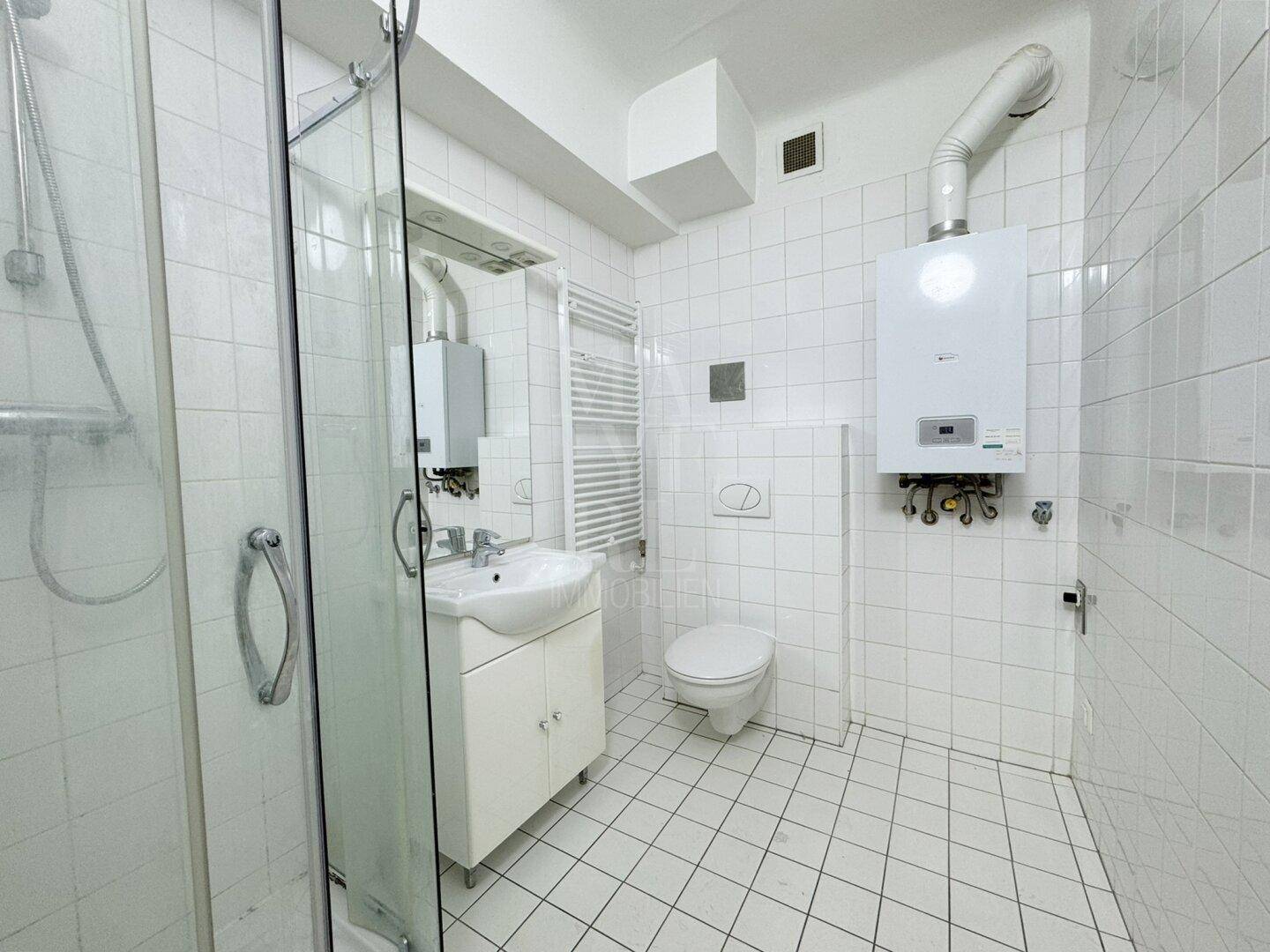 Funktionales Badezimmer mit weißen Fliesen, Duschkabine, WC und Waschbecken.