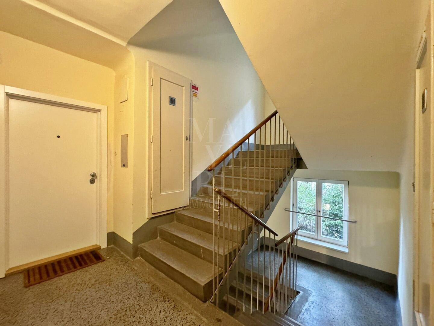 Treppenhaus eines Mehrfamilienhauses mit Fenster und Zugang zu den Wohneinheiten.