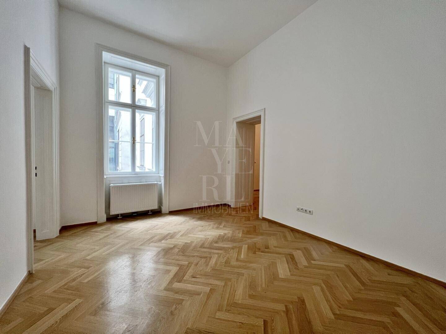 Heller Raum mit elegantem Fischgrätparkett und einem großen Fenster, das viel natürliches Licht spendet.