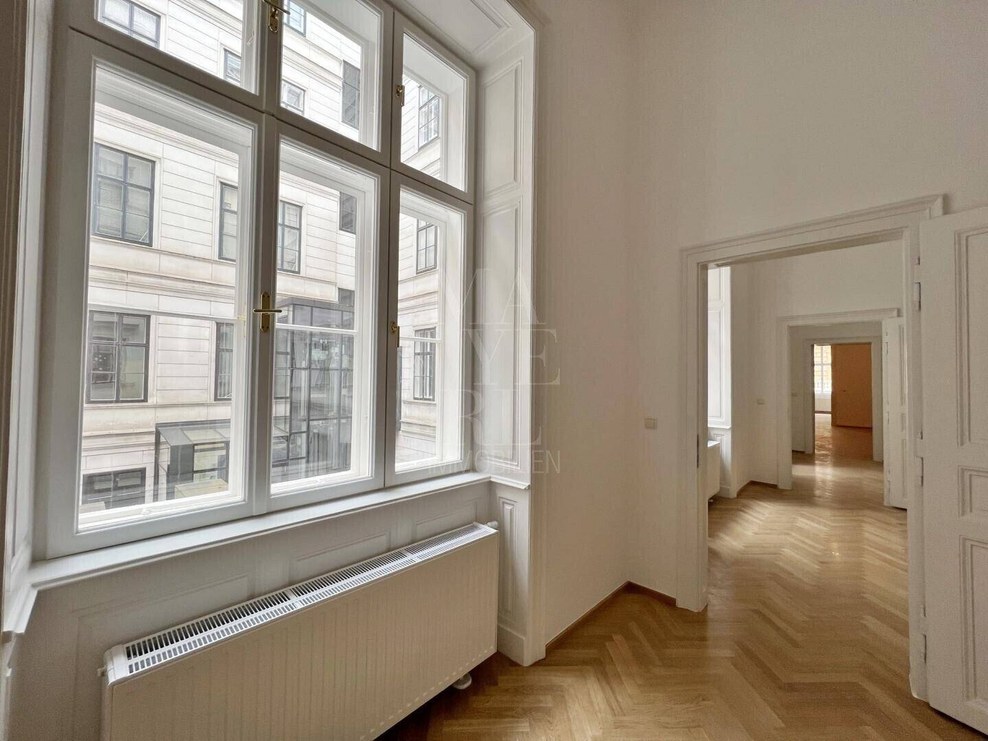 Großes Fenster mit Heizkörper und Blick auf die historische Fassade eines gegenüberliegenden Gebäudes.