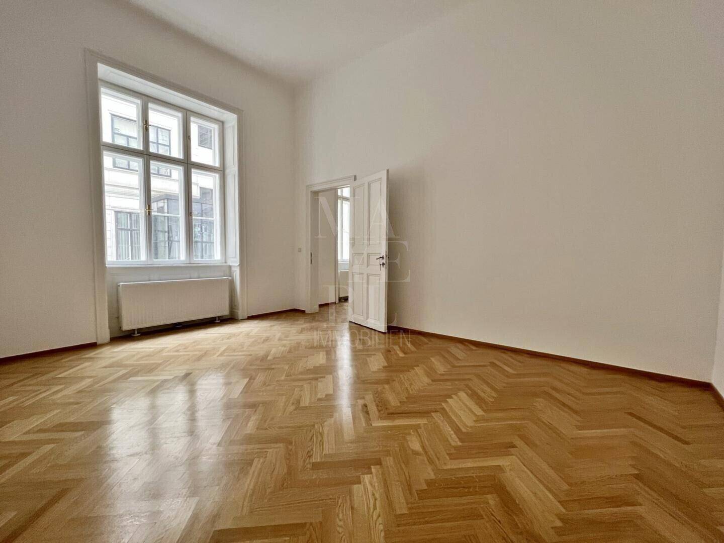 Heller, leerer Raum mit glänzendem Fischgrätparkett und hohen Wänden, bereit für individuelle Gestaltung.