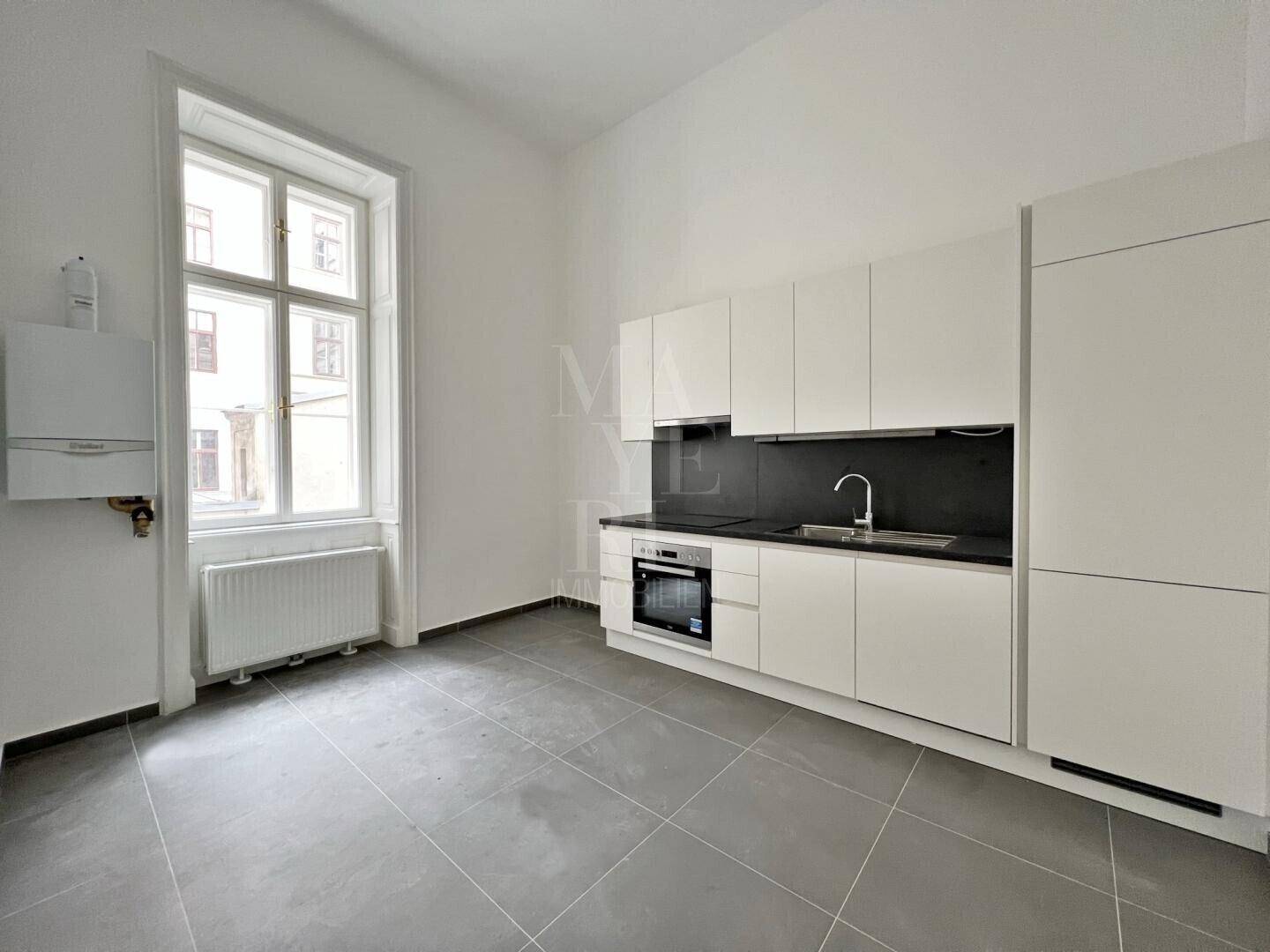 Moderne Küche mit weißen Hochglanzschränken, schwarzer Arbeitsplatte und integrierten Geräten.