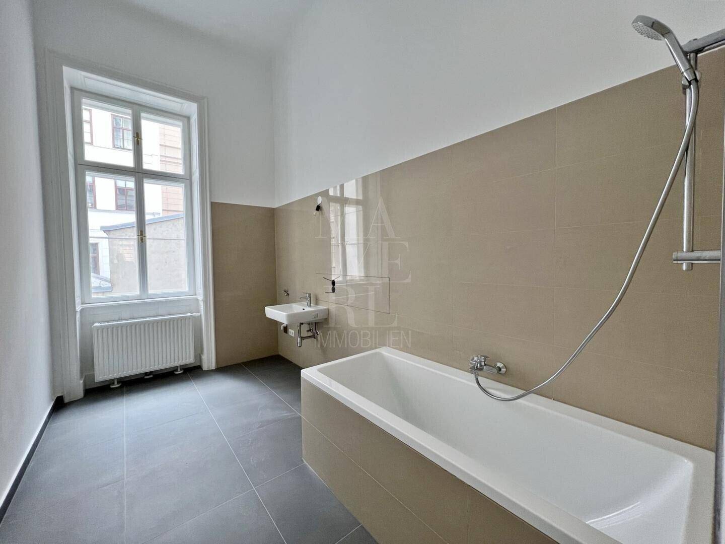Modernes Badezimmer mit Badewanne, Einzelwaschbecken und großen Fliesen in neutralen Farbtönen.