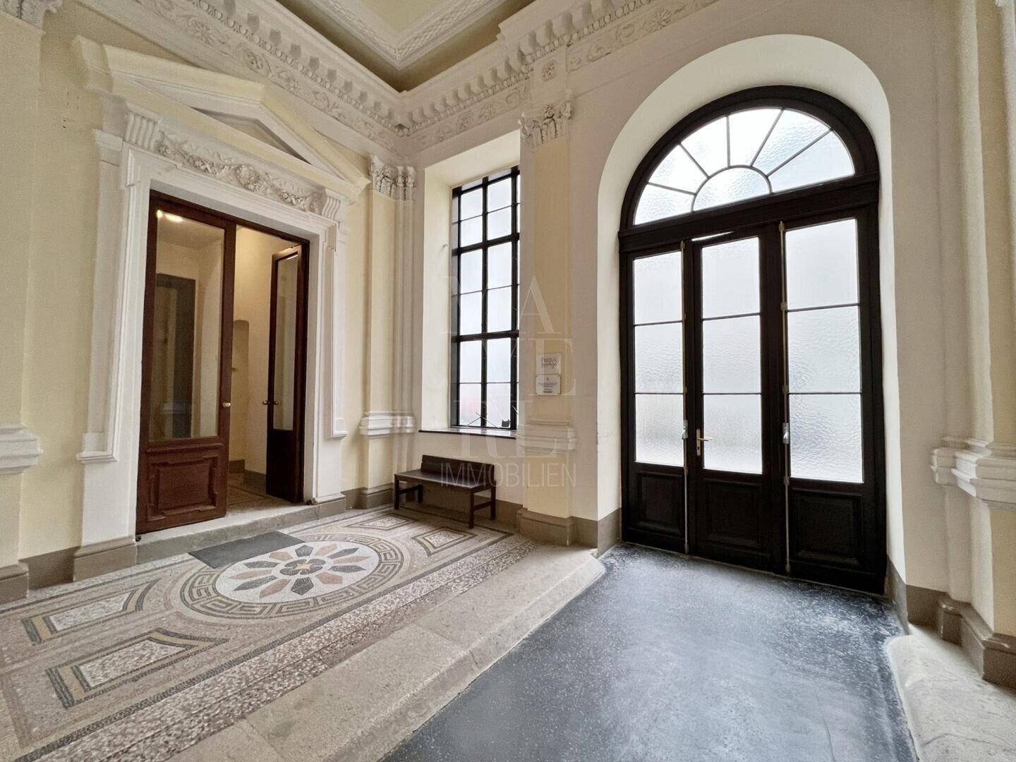 Repräsentativer Eingangsbereich mit kunstvollem Mosaikboden und hohen, gewölbten Fenstern.