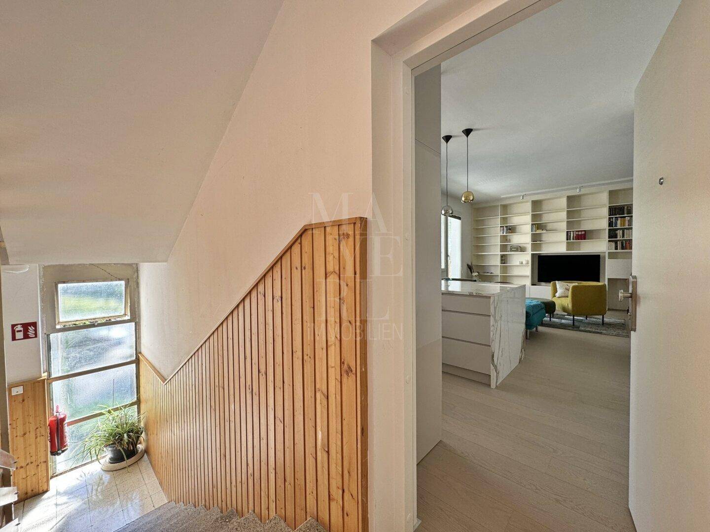 Treppenhaus mit Holzverkleidung, das zum hellen und offenen Wohnbereich der Wohnung führt.