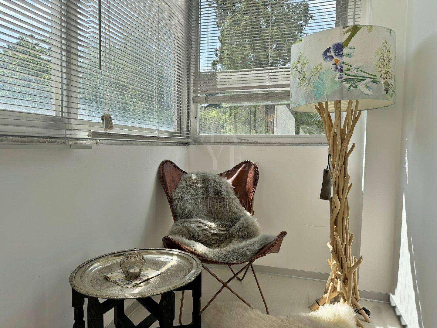 Gemütliche Ecke mit Sessel, Beistelltisch und dekorativer Stehlampe, umgeben von großen Fenstern.