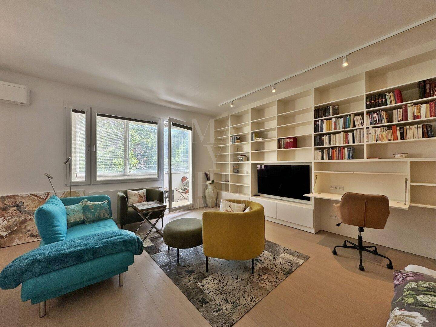 Geräumiges Wohnzimmer mit bequemen Sitzmöbeln, großem Bücherregal und Zugang zum Balkon.