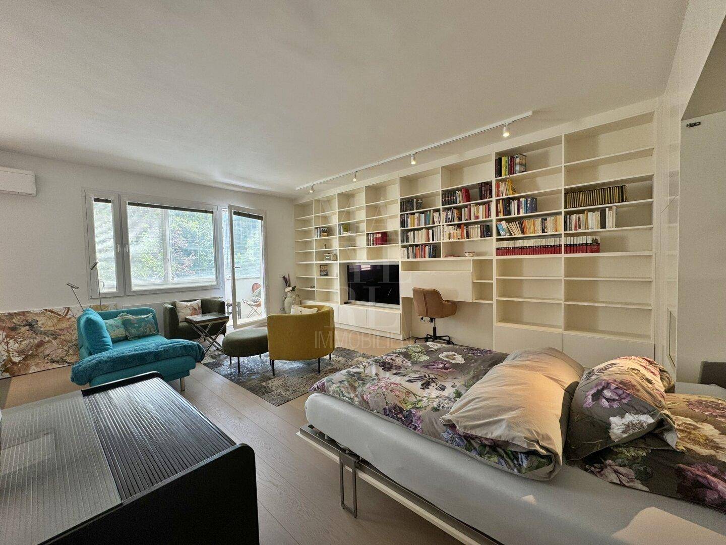 Heller Wohnbereich mit ausklappbarem Bett, großem Bücherregal und Zugang zu einem Außenbereich.