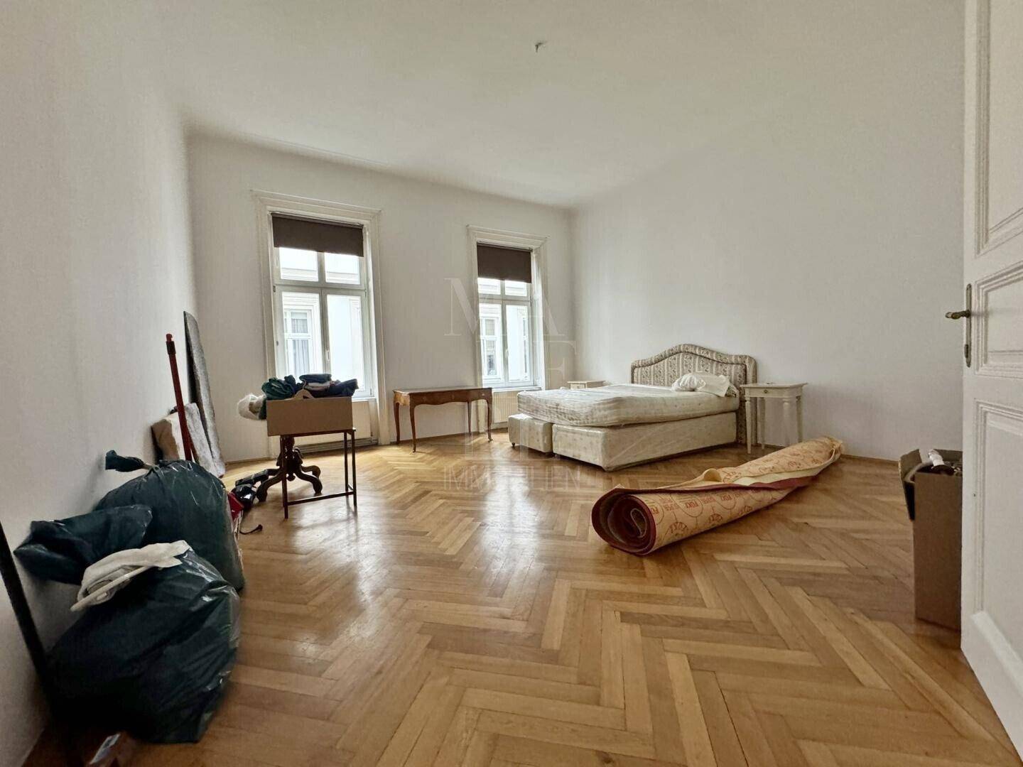 Schlafzimmer mit Fischgrätparkett, hohen Fenstern und einem Doppelbett.