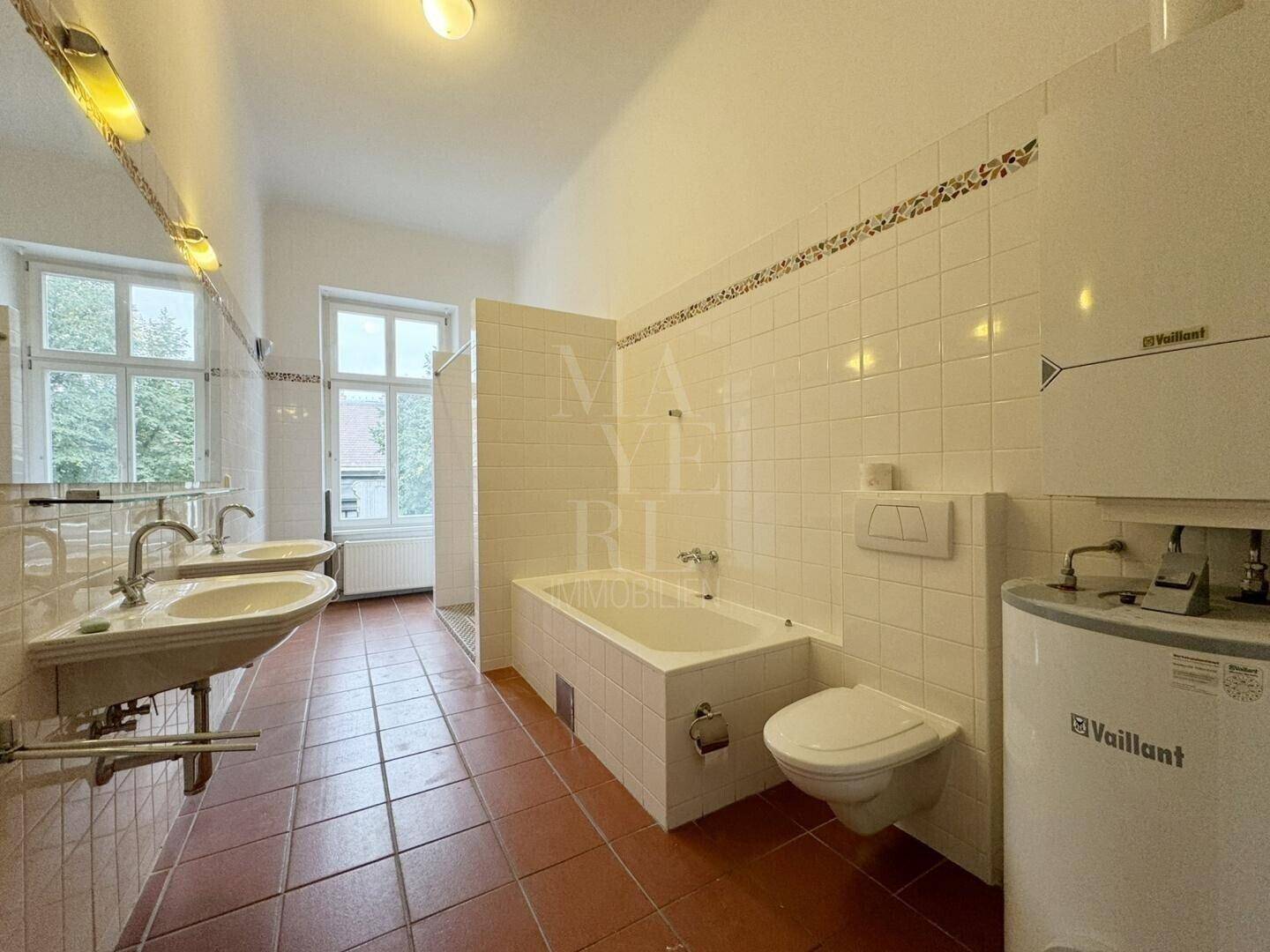 Geräumiges Badezimmer mit zwei Waschbecken, Badewanne, WC und Terrakottafliesen.