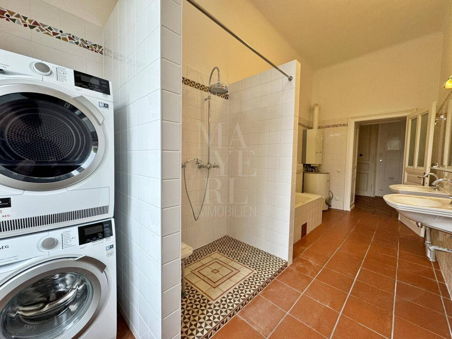 Badezimmer mit Duschbereich, Waschmaschine, Trockner und zwei Waschbecken.