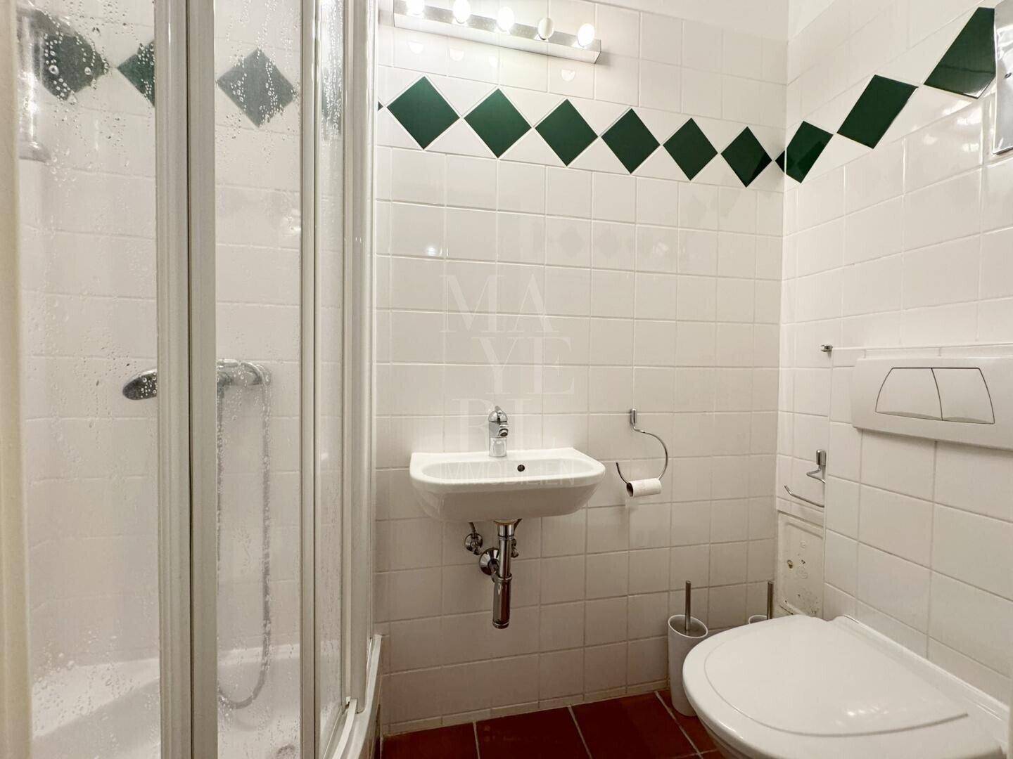 Kleines Badezimmer mit Dusche, WC und Waschbecken, dekoriert mit grünen Fliesen.