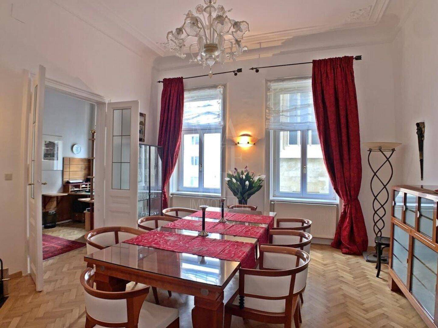 Elegantes Esszimmer mit großem Holztisch, Parkettboden und dekorativen roten Vorhängen.