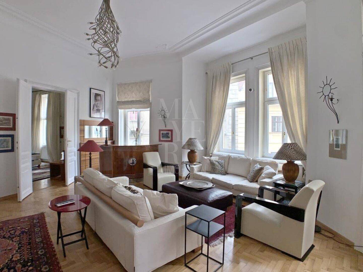 Geräumiges Wohnzimmer mit klassischem Parkettboden, hohen Decken und großen Fenstern.