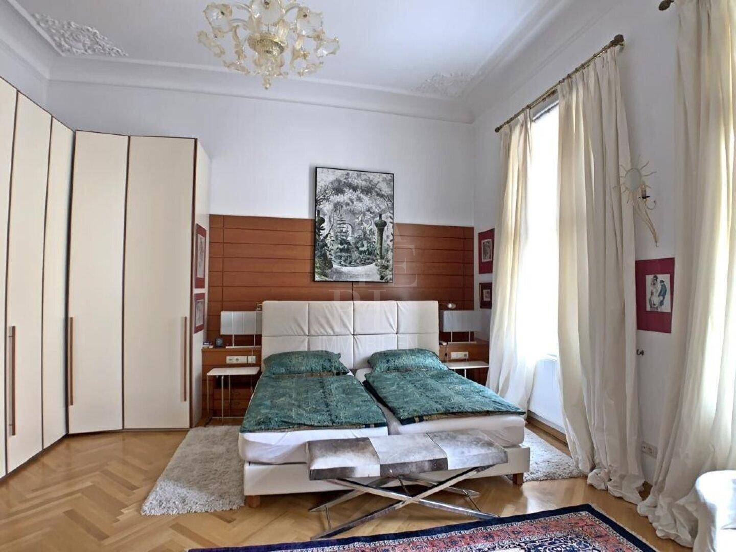 Helles Schlafzimmer mit Parkettboden, hohen Decken und großen Einbauschränken.