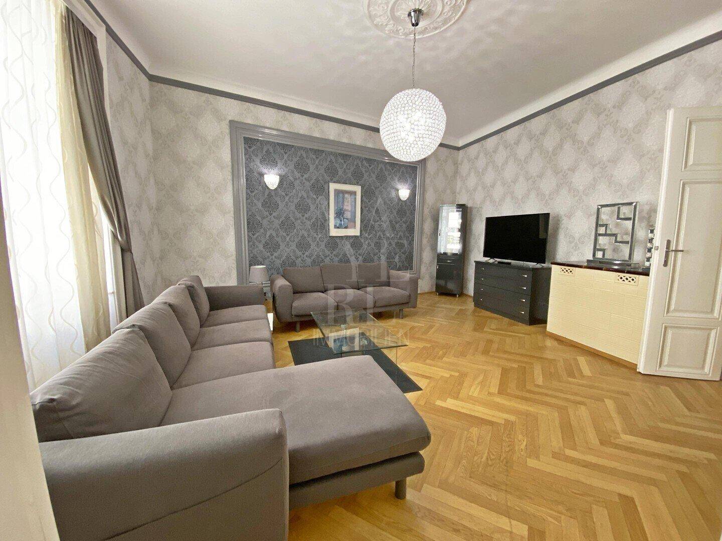 Helles Wohnzimmer mit bequemen Sofas, Fischgrätparkett und dekorativer Wandgestaltung.