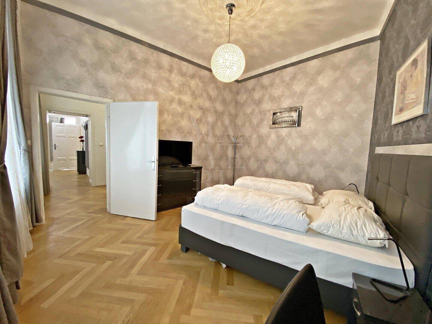 Schlafzimmer mit Fischgrätparkett und Zugang zu weiteren Räumen, hell und geräumig.