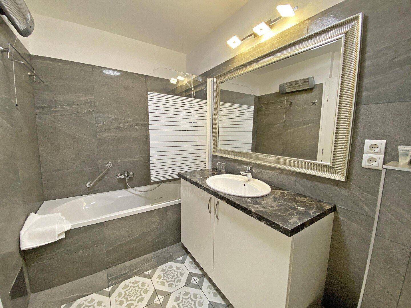 Modernes Badezimmer mit Badewanne, Einzelwaschbecken und gemusterten Bodenfliesen.