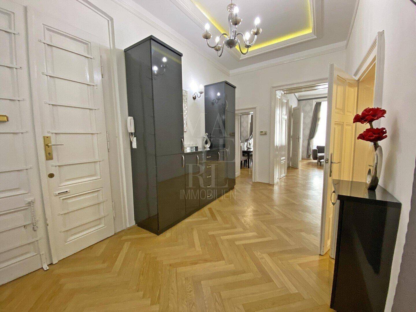Geräumiger Eingangsbereich mit Fischgrätparkett, hohen Decken und eleganten Schränken.