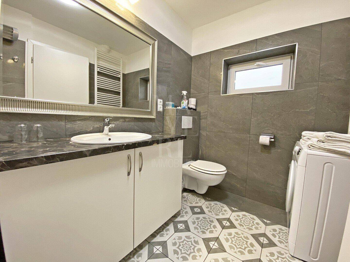 Badezimmer mit WC, Waschmaschine, Einzelwaschbecken und Fenster für Tageslicht.
