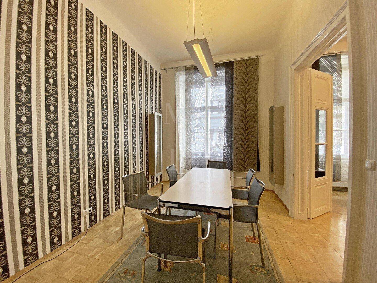 Esszimmer mit langem Tisch, modernen Stühlen und dekorativer Tapete.